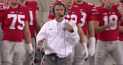Sports gif. Urban Meyer, coach for the Ohio State Buckeyes, puts his hands on his head and leans way back in frustration. The players behind him look on in disbelief.