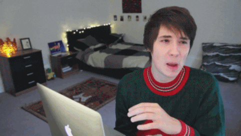 Video gif. YouTuber Dan Howell physically cringes and grimaces at something on his laptop, squeezing his eyes shut and blocking his screen with his hand.