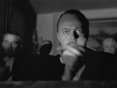 Movie gif. Joseph Cotten as Jedediah Leland in "Citizen Kane" sits among an audience, frowning and clapping very sternly.