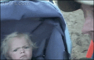 Video gif. A blonde baby in a stroller looking over at someone with suspicion.