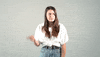 Video gif. A woman stares at us with a concerned look and then bounced a finger off her head like she’s calling us dumb. 