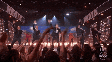 TV gif. New Kids on the Block performing at the 2021 American Music Awards, the five members swaying and waving their arms side to side in unison with the crowd.