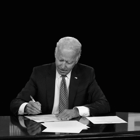 Political gif. Joe Biden seated at his desk, signing papers, an aqua arrow pointing diagonally in a downward trend and white marker font appears reading, "Under Biden, the deficit dropped the most in US history."