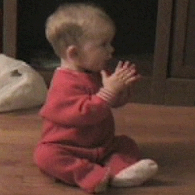Video gif. A baby is sitting on the floor and gently and slowly claps its hands.