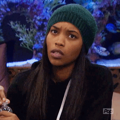 Reality TV gif. Woman from Big Brother After Dark gives a confused facial expression. She wears a knit hat and has straight, dark hair, and a fish tank is visible in the background.