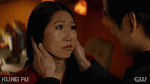 TV gif. Shannon Dang as Althea on Kung Fu smiles slightly, heartened, at Tony Chung as Dennis, who cradles her face with his hands and then embraces her.