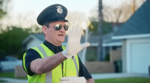 Music Video gif. Brett Eldredge's music video for Somethin' I'm Good At. A crossing guard raises his hand up and stops the cars as he reaches for his whistle.