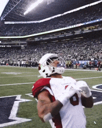 Sports gif. James Conner of the Cardinals kneels in the endzone. He pulls his hands down in front of his helmet in prayer as he shakes his head with gratitude. His teammates run up behind him and give him victorious pats on the shoulders and helmet.