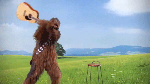 Star Wars gif. Chewbacca appearing in a spacious landscape, smashing an acoustic guitar on a stool.