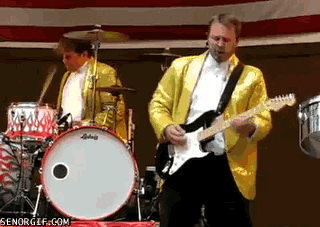 Video gif. Drummer in a band goes absolutely crazy as he plays, hitting the cymbals hard and thrashing his arms and head around. Next to him, the guitarist plays and vibes.