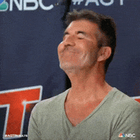 Reality TV gif. Simon Cowell on America’s Got Talent has an embarrassed smile spread across his face. He has his eyes closed and he face palms into his hands in disappointment. 
