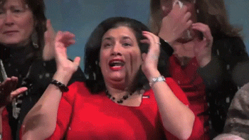 Video gif. Woman in a bright cherry red dress and matching lipstick runs her hands through her hair and screams in panic. Other women behind her are wiping away tears and blowing their noses, and snow begins to fall upon them.