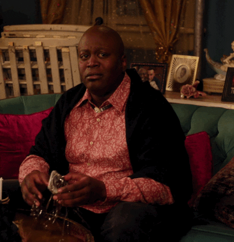 TV gif. Tituss Burgess as Titus on The Unbreakable Kimmy Schmidt looks concerned as he glances at someone. He does the sign of the cross and then adds some hand motions and a dance to it. 