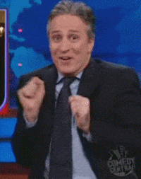 TV gif. Jon Stewart on The Daily Show restless, wide-eyed and giddy, clapping his hands.