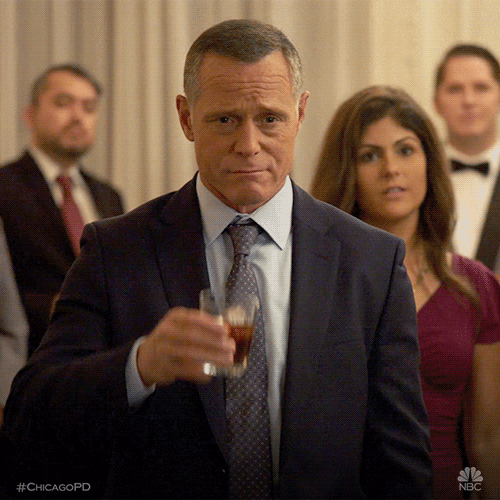 TV gif. Jason Beghe as Hank in Chicago PD somberly raises a whiskey drink in tribute. 