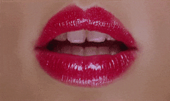Video gif. A pair of dark pink lipsticked-lips smooches toward the camera.