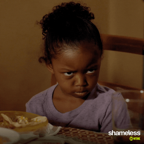 TV gif. Amirah Johnson as Xan from Shameless sits at the dinner table and looks up at someone, brow furrowed in displeasure.