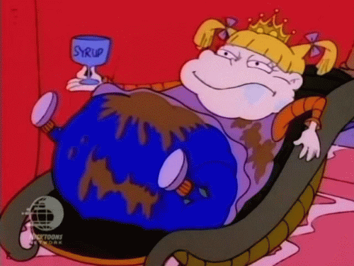 Cartoon gif. Angelica on the Rugrats sits on a throne with a crown on her head. She’s fat with her feet up in the air, brown syrup splattered all over her body. She chews on something with drool coming out of her mouth, holding a goblet that says “Syrup."