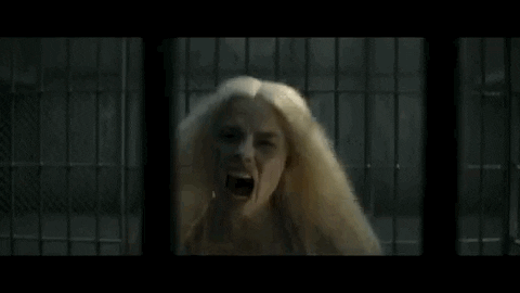 Movie gif. Margot Robbie as Harley Quinn in Suicide Squad runs towards us in her large cage-like jail cell. She screams and then bangs her head straight into the metal bar.