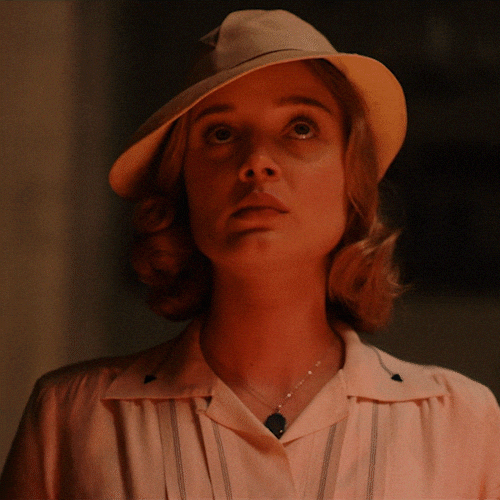 TV gif. Wearing a beige hat and lit by candlelight, Susan Parsons as Bella Heathcote from Strange Angel lowers her head, closes her eyes, and blesses herself with the sign of the cross.