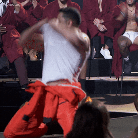 Sponsored gif. Jonathan Johnson, a contestant on The Bachelorette, kneels down on stage and rips his own shirt off of his chest like he's doing a strip tease on a continuous loop. Other male contestants sit in the background, watching and cheering him on.