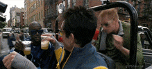 Movie gif. Ben Stiller as Derek in Zoolander drives in his jeep with his model friends dancing round joyfully and toasting their orange mocha frappuccinos. 
