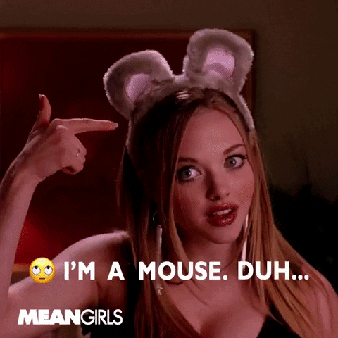 Movie gif. Door opens on Lacey Chabert as Gretchen in Mean Girls as she poses in a low cut leather costume, then asks Amanda Seyfried as Karen, "What are you?" Karen shows off her lingerie-like costume and replies, "I'm a mouse. Duh," as she points to her mouse ear headband.
