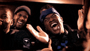 Video gif. Sitting in an audience, four men react to something in amusement, laughing and clapping, but suddenly their expressions change to shocked anger as one of the men sits up and says, “What the fuck?!”