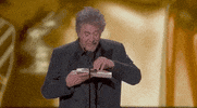 Oscars 2024 GIF. Like someone opening a candy wrapper, Al Pacino slowly unpeels the award envelope, and his eyes widen in excitement. He says, "My eyes see Oppenheimer."
