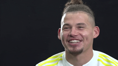 Sports gif. Kalvin Phillips squints his eyes and smiles, pointing at something to the left.