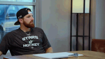 Video gif. A bearded man sits at the head of a table throws a pen and pops his hands to his face in clear frustration.