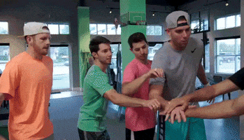 Reality TV gif. Members of The Dude Perfect Show place a hand on top of one another's as a sign of team work. They chant together then toss their hands up in unison. 