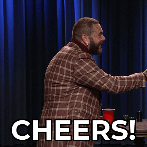 TV gif. On The Tonight Show, Post Malone clinks a shot glass with someone out of frame and then raises the glass toward us, smiling. Text, "cheers!"