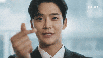 Video gif. Closeup of Choi Jun-woong looks at us with a smile and holds two thumbs up in front of the camera.