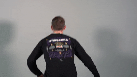 Video gif. Man jumps and turns towards us, landing with two thumbs up and a sarcastic expression on his face.