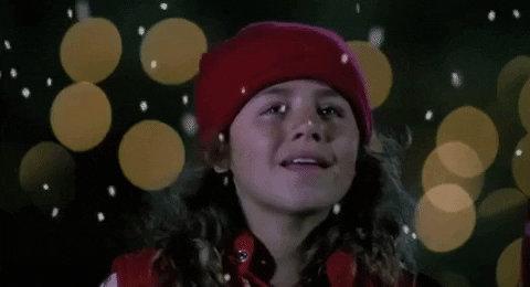 Movie gif. Brown-haired girl in a read cap looks up and smiles as snow falls around her in "The Santa Clause."