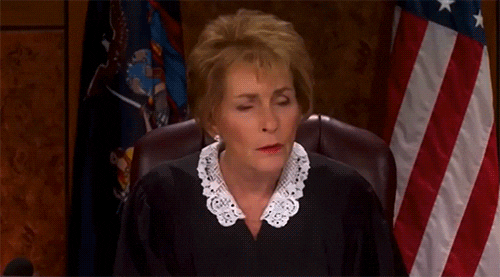 Reality TV gif. Judge Judy looks down from her stand with a questioning expression on her face. She leans forward to hear better.