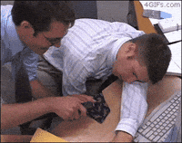 Video gif. Two men are in an office and one is asleep at his desk. The other staples the sleeping man's tie to the desk then slaps him awake. The man jolts awake and tries to attack his friend but gets caught by the staple and falls down.