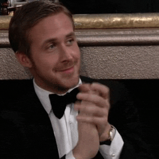 Celebrity gif. Ryan Gosling wears a tux at an awards ceremony as he claps with a knowing smile on his face.