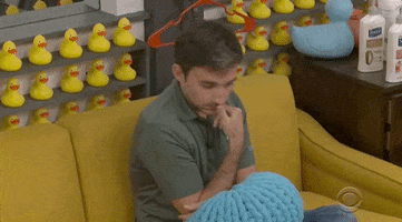 Reality TV gif. Ian from Big Brother holds a finger up to his mouth as he rocks back and forth on a couch. 