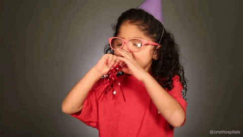 Video gif. Young girl with big, pink glasses and a purple party hat on her head blows into a party noisemaker really hard. She then smiles, taking it out of her mouth, and holds it in her hands while laughing.