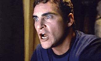 Movie gif. Joaquin Phoenix as Merrill in Signs. He sees something on his computer that utterly shocks him, and he throws a hand over his mouth before standing and backing up. He backs up so far, he hits the end of his room, and he bends over in shock.