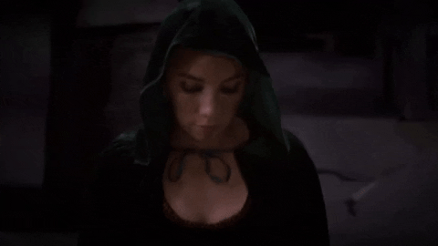 Music video gif. In a clip from the Fall Out Boy music video, "Love from the other side," a woman wears a hooded cloak as she approaches with her head down then gazes up with a modest expression.