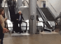 Political gif. We follow Bernie Sanders as he steps off of an escalator and jogs past several people.