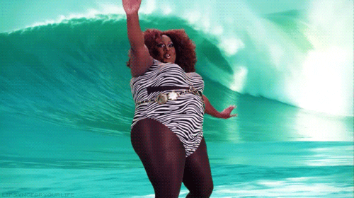Video gif. A confident fat woman with a big afro reels and regains her balance as she surfs on an artificial surfboard.