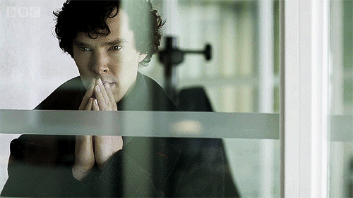 TV gif. Benedict Cumberbatch as Sherlock Holmes sits behind a window as presses his hands together in deep thought, scheming up something.