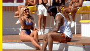 Reality TV gif. Mady McLanahan and Jeff Christian Jr. from Love Island sit alongside the edge of a pool and raise their hands to high five but miss.