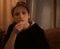 Celebrity gif. Sarah Michelle Gellar as Buffy Summers in Buffy the Vampire Slayer puts a piece of popcorn in her mouth, her expression blank.