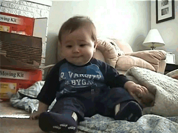 Video gif. A happy baby boy belly laughs until he tips over. 