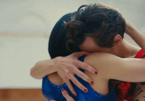 Music video gif. From the As it Was video: Looking sad and concerned, a tattooed Harry Styles hugs a woman, then pulls away, locking eyes with her in a moment of emotional intimacy.